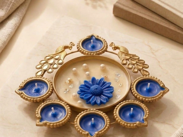 Gold peacock metal diya platter with sky blue wax candles and central pearl flower dish